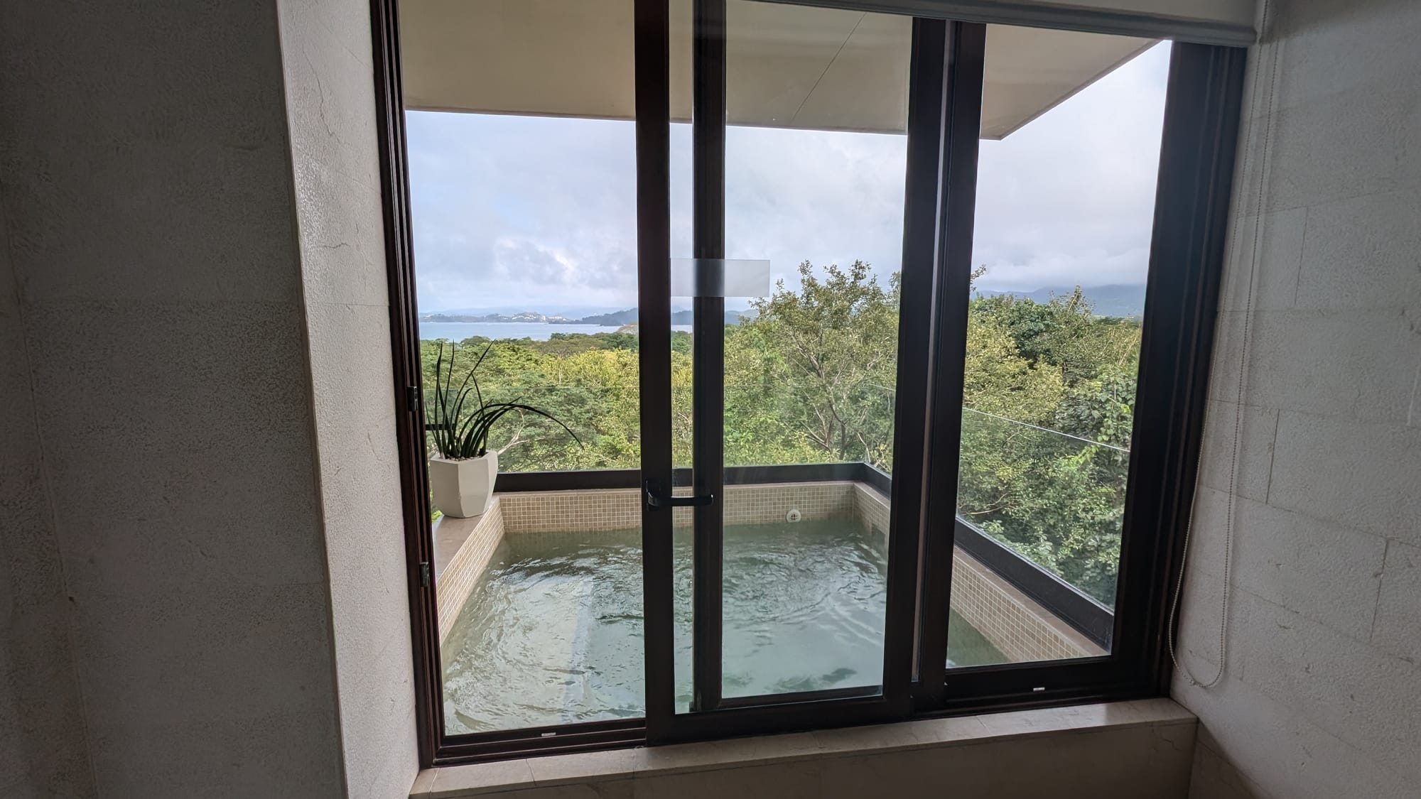 View of the outdoor balcony hot tub, jungle and ocean from inside the double rain shower of our suite at the W Conchal 