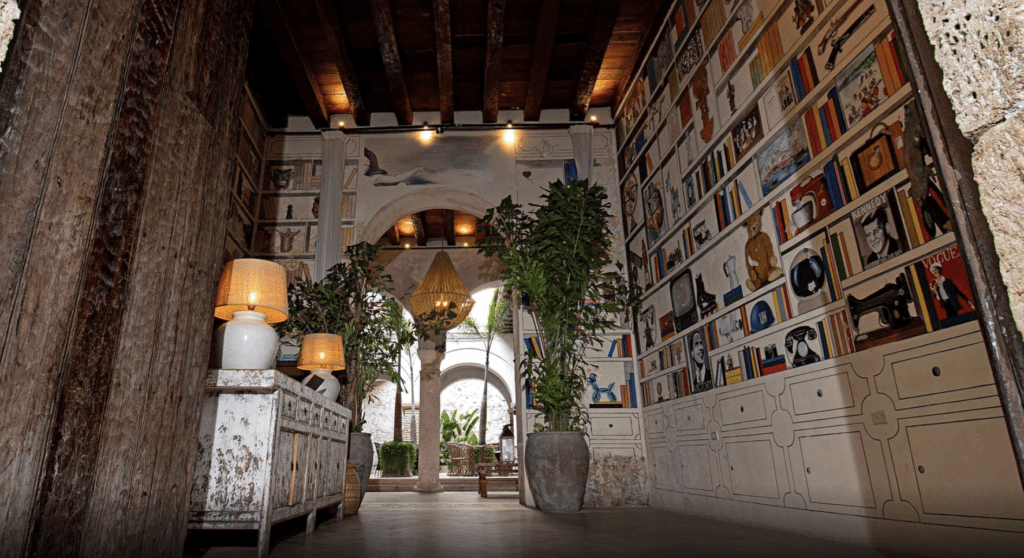 a room with a wall of books and a table with lamps