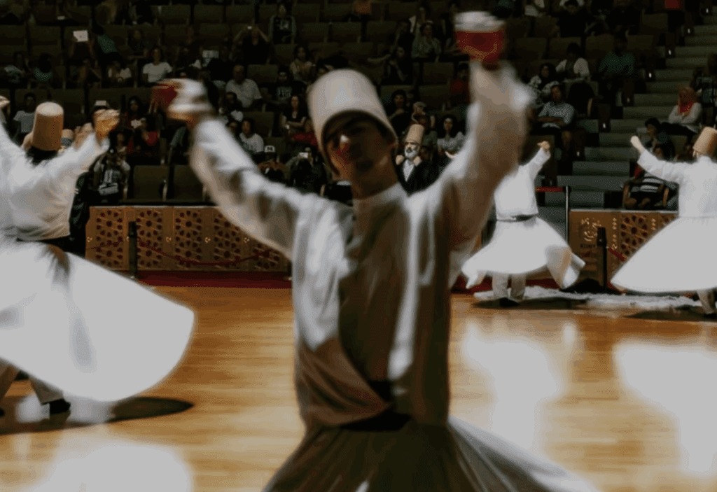 a man wearing a white robe and holding cups in front of a crowd